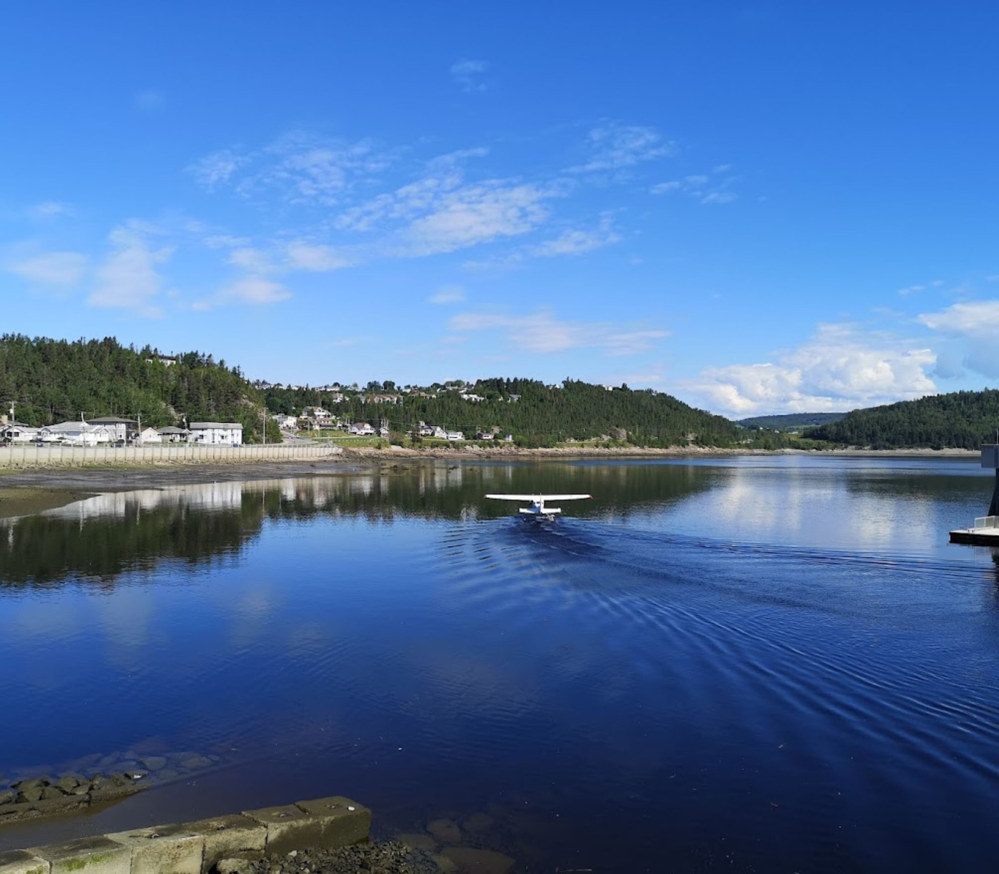 A calm lake with a small boat, a dock, and a forested hillside in the background.
