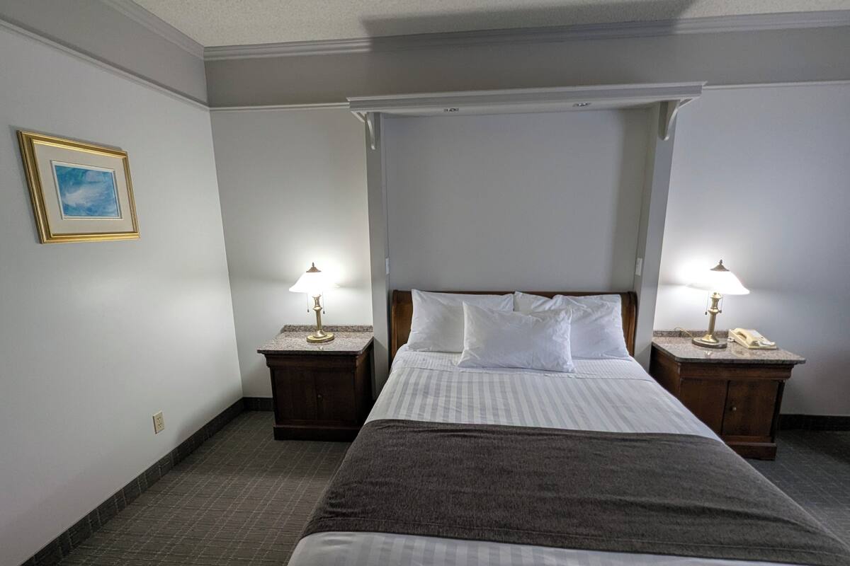 A hotel room with a large bed, two bedside tables with lamps, a framed picture on the wall, and a carpeted floor.