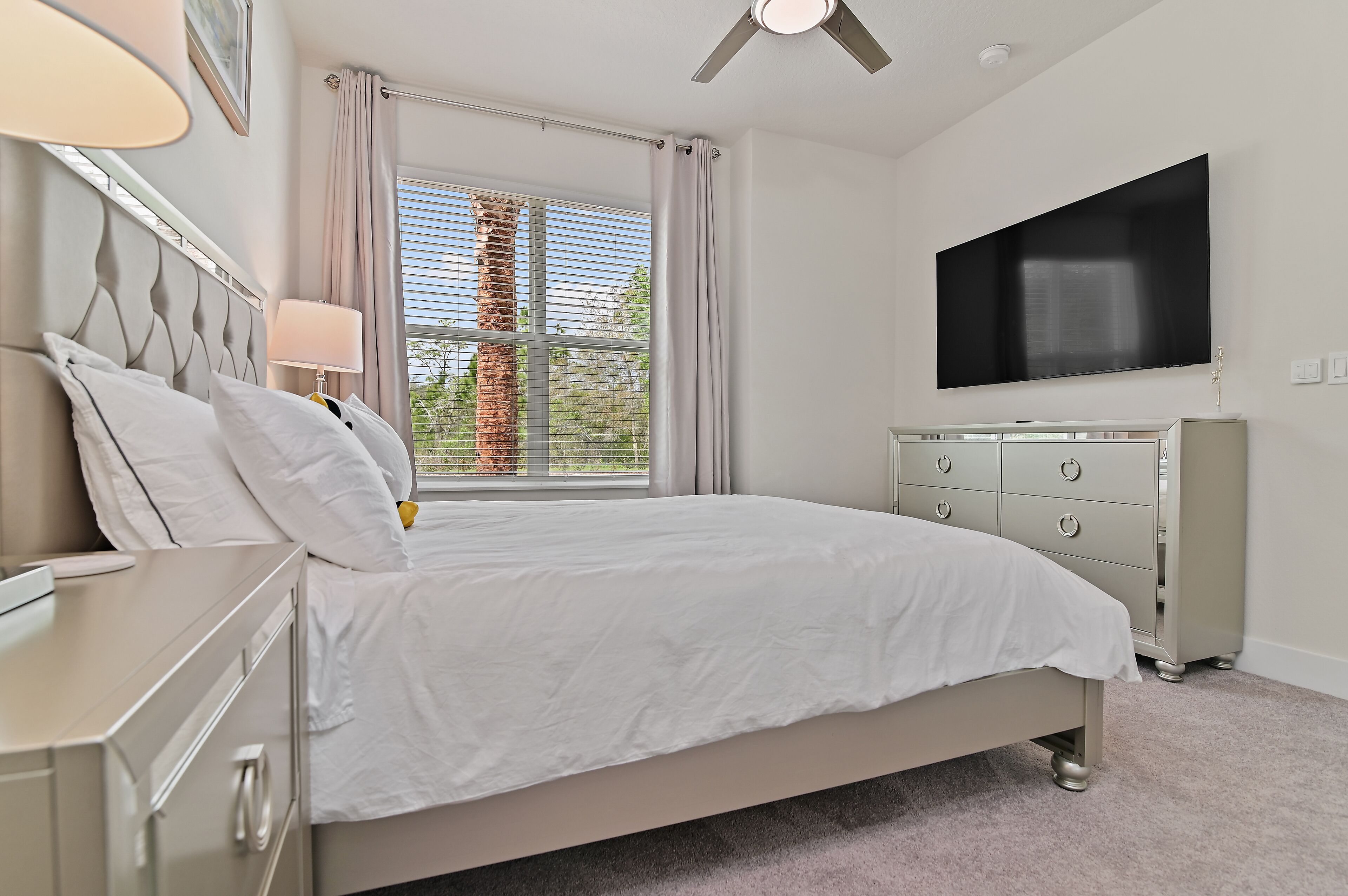 A bedroom with a bed, a dresser, a TV, and a window with curtains.