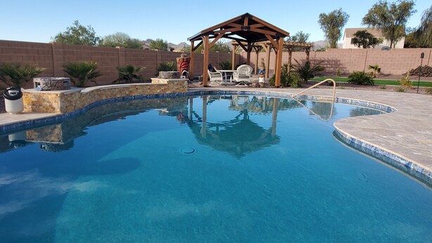 Una piscina cristalina con cubierta de madera y sillas de descanso, rodeada por un muro de piedra y plantas en macetas.