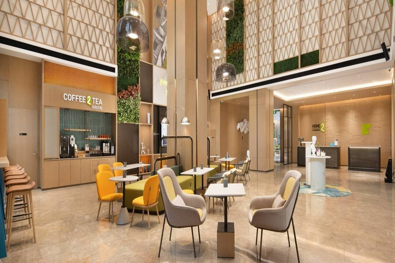 Un espacio interior moderno con zonas de estar, una cafetería y un mostrador de recepción.