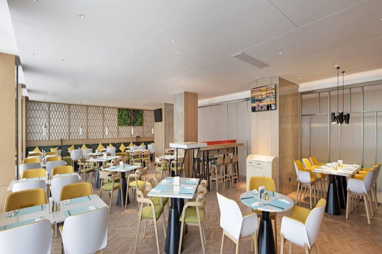 A modern dining area with multiple tables and chairs, a kitchen area, and a decorative wall.