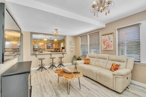 Un salon avec un canapé beige, des tables basses en bois et un lustre.