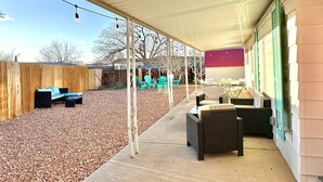 Un patio couvert aménagé avec du mobilier d’extérieur, une clôture en bois et un mur en briques rouges.