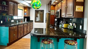 Une cuisine moderne avec des meubles en bois, un plan de travail noir et un luminaire suspendu aux couleurs vives.