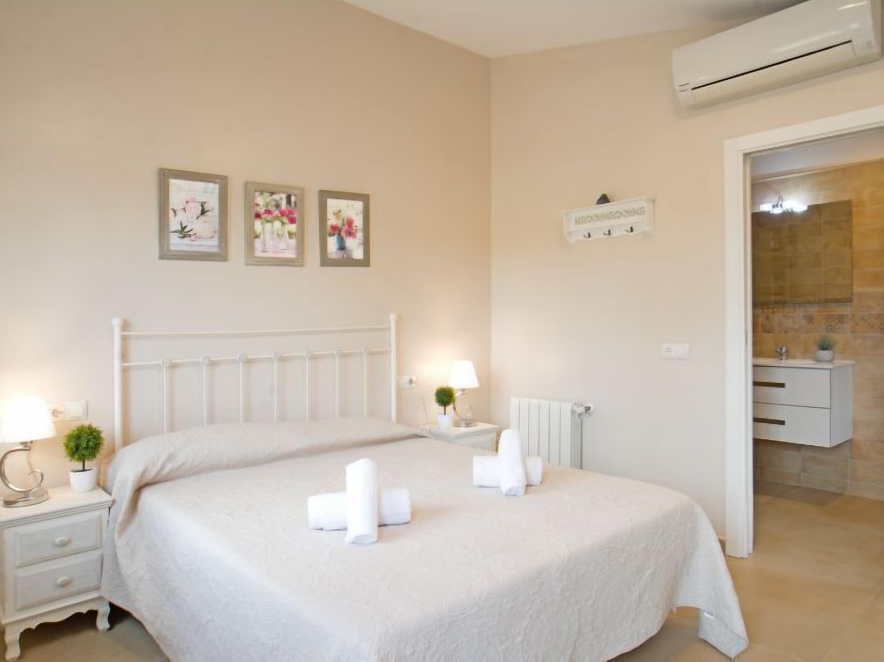 Une chambre d’hôtel avec un grand lit, une table de chevet avec une lampe et une petite plante en pot. On aperçoit une salle de bain à travers une porte ouverte.