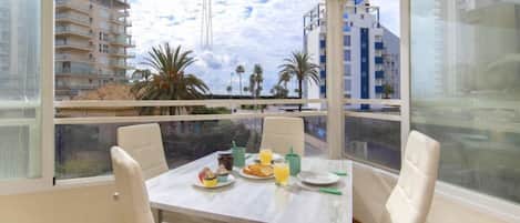 Un comedor con una mesa dispuesta para dos personas, con vistas a un paisaje urbano con edificios modernos y palmeras.