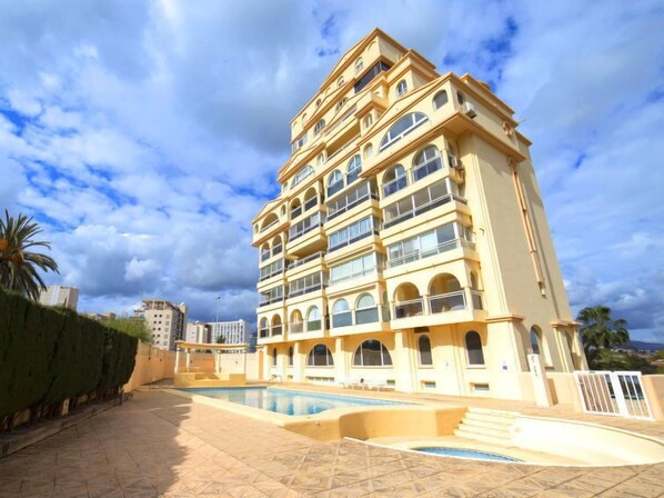 A multi-story hotel with a pool area, featuring balconies and a Mediterranean architectural style.
