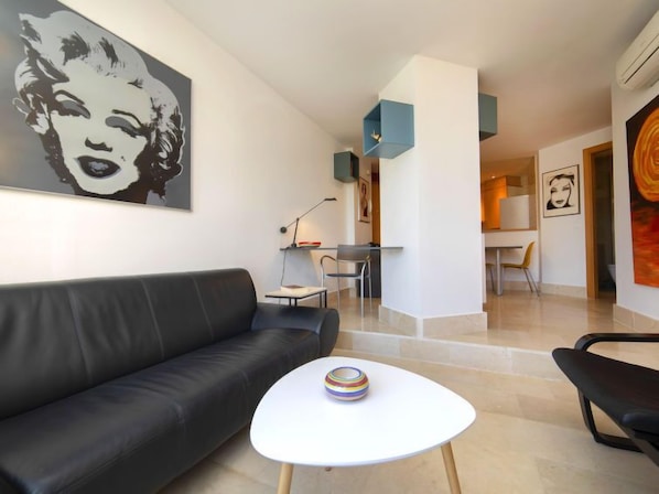 A modern living room with a black leather sofa, a white coffee table, and a large black and white portrait on the wall.