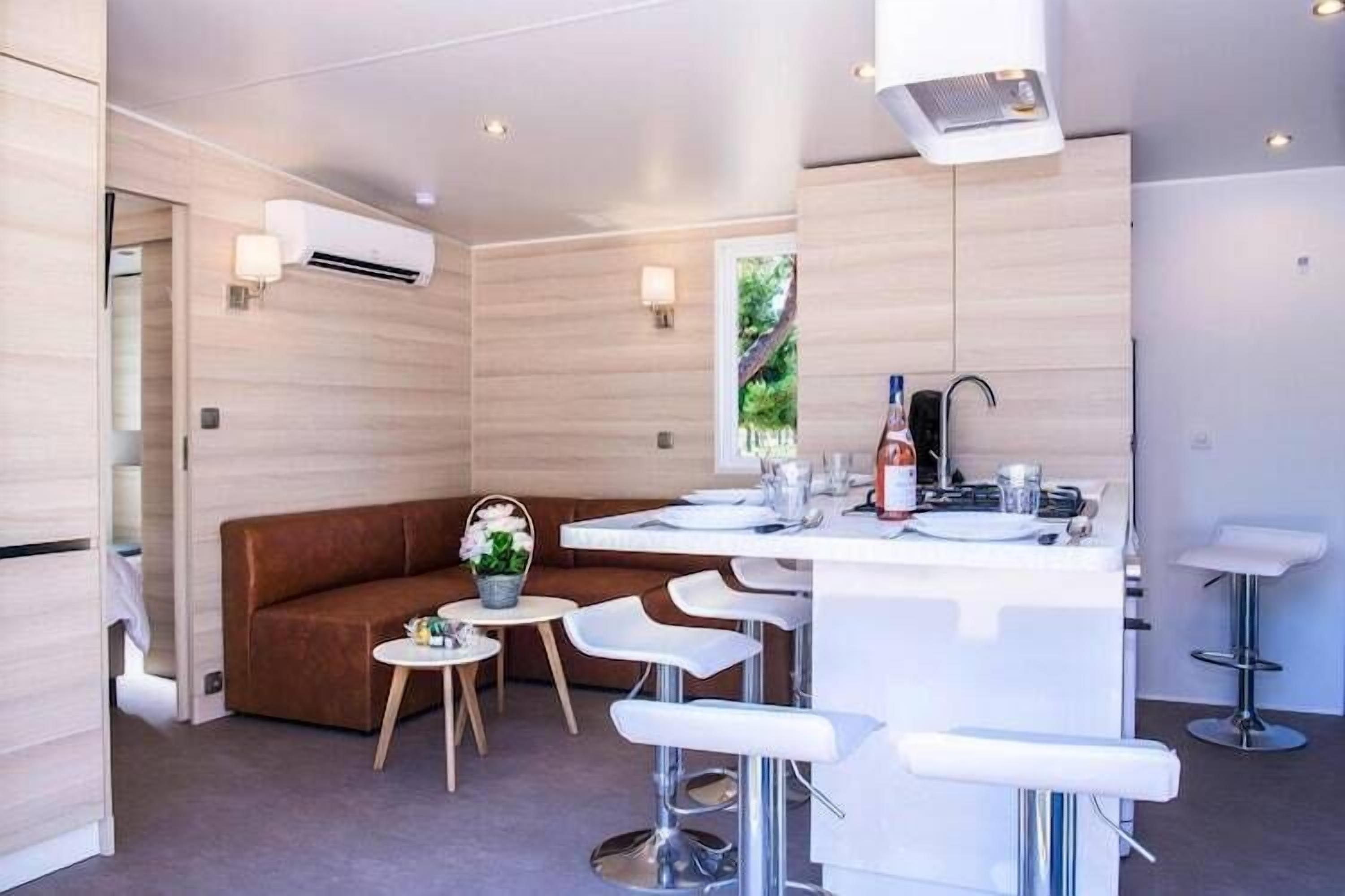Uma cozinha moderna com uma ilha central, banquetas, um sofá marrom e uma pequena mesa redonda com um vaso de flores.