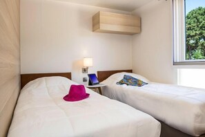 Two single beds with white duvets, a bedside table, and a window with a view of the surrounding trees.