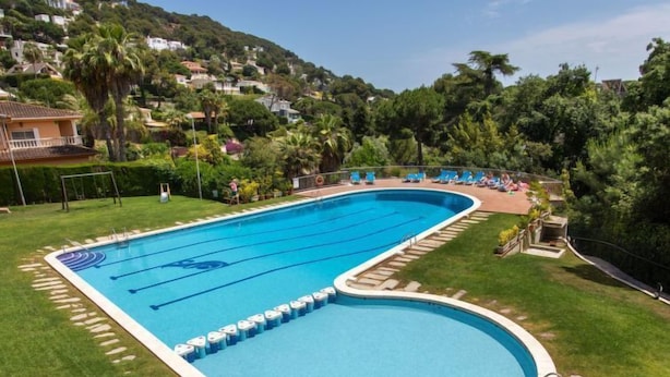 Ein großer, rechteckiger Schwimmteich mit mehreren Bahnen, umgeben von einer Rasenfläche und einer ansteigenden Landschaft im Hintergrund.