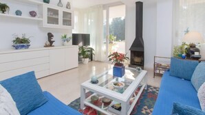 Ein Wohnzimmer mit einer Couch, einem Couchtisch und einem Kamin. Regale mit Dekorationselementen und ein Fernseher sind ebenfalls vorhanden.