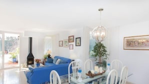 Ein helles Wohnzimmer mit einem blauen Sofa, einem Glastisch mit weißen Stühlen, einem schwarzen Kamin und einer Chandelüster.