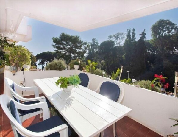 An outdoor patio with a white table and chairs, surrounded by potted plants and trees. - Cala Bona by Interhome (Blanes)