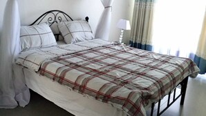 A bed with a plaid bedspread, white pillows, and a canopy. - Beach apartment on Kenyan coast. (Kilifi)