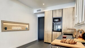 A modern kitchen with a wooden accent wall, built-in ovens, a coffee machine, and a cutting board with bread. - N&J - BLUE PROMENADE - Sea front - central - Luxe (Niza)