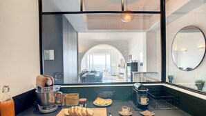 A modern kitchen with a large window, a coffee machine, a cutting board with bread, and a coffee cup. - N&J - BLUE PROMENADE - Sea front - central - Luxe (Niza)