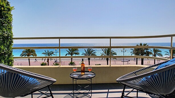 A balcony with two chairs and a small table, overlooking a beach with palm trees and the ocean. - N&J - BLUE PROMENADE - Sea front - central - Luxe (Niza)