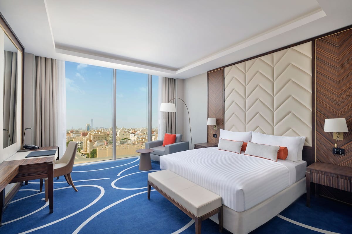 Une chambre d’hôtel avec un grand lit, un bureau, une chaise, un banc et une vue sur la ville.