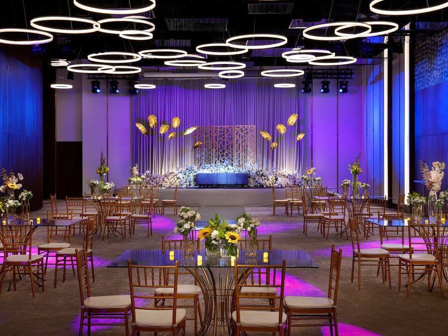 A banquet hall with round tables, chairs, and a stage with floral arrangements.