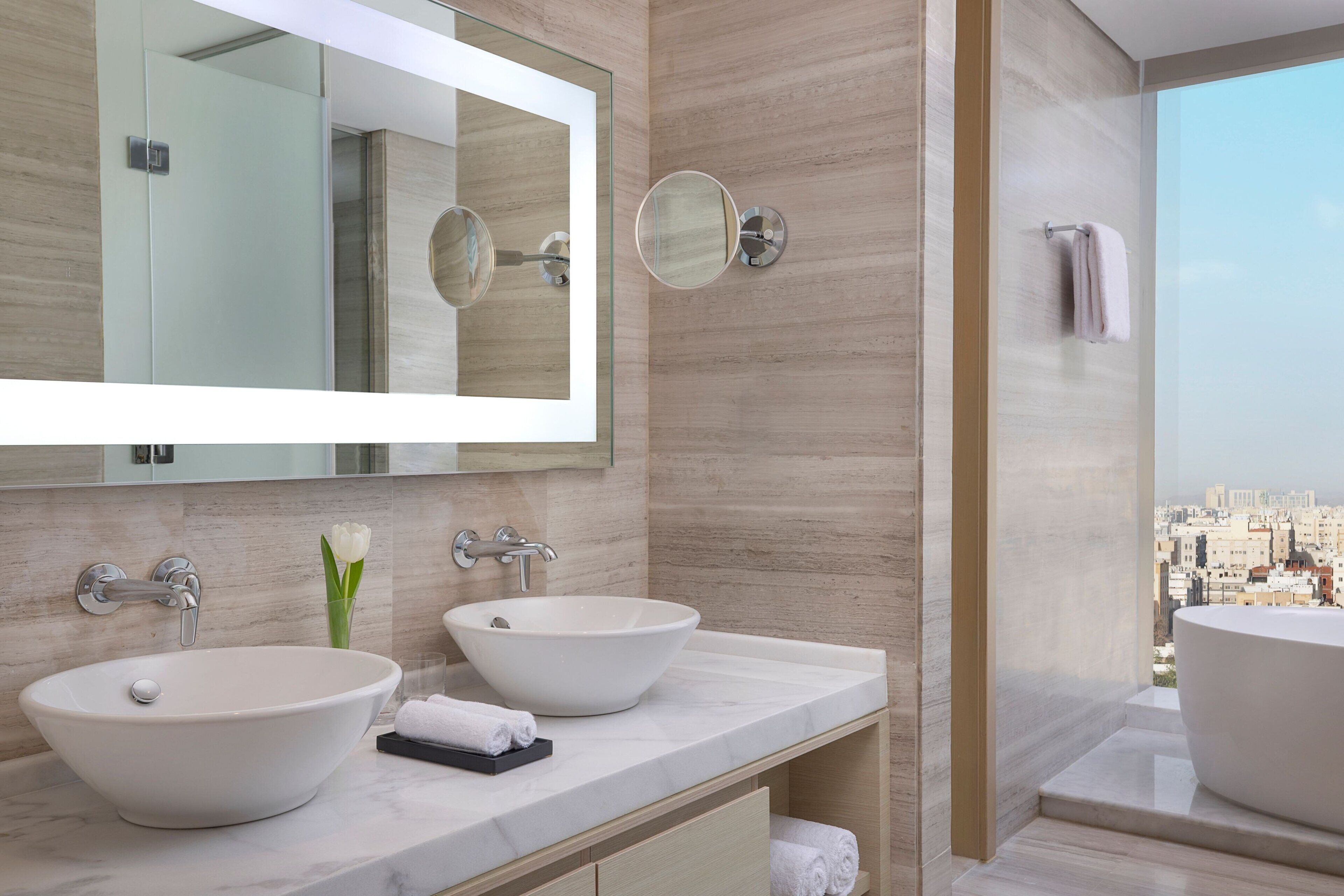 A modern bathroom with two vessel sinks, a large mirror, and a view of the city.