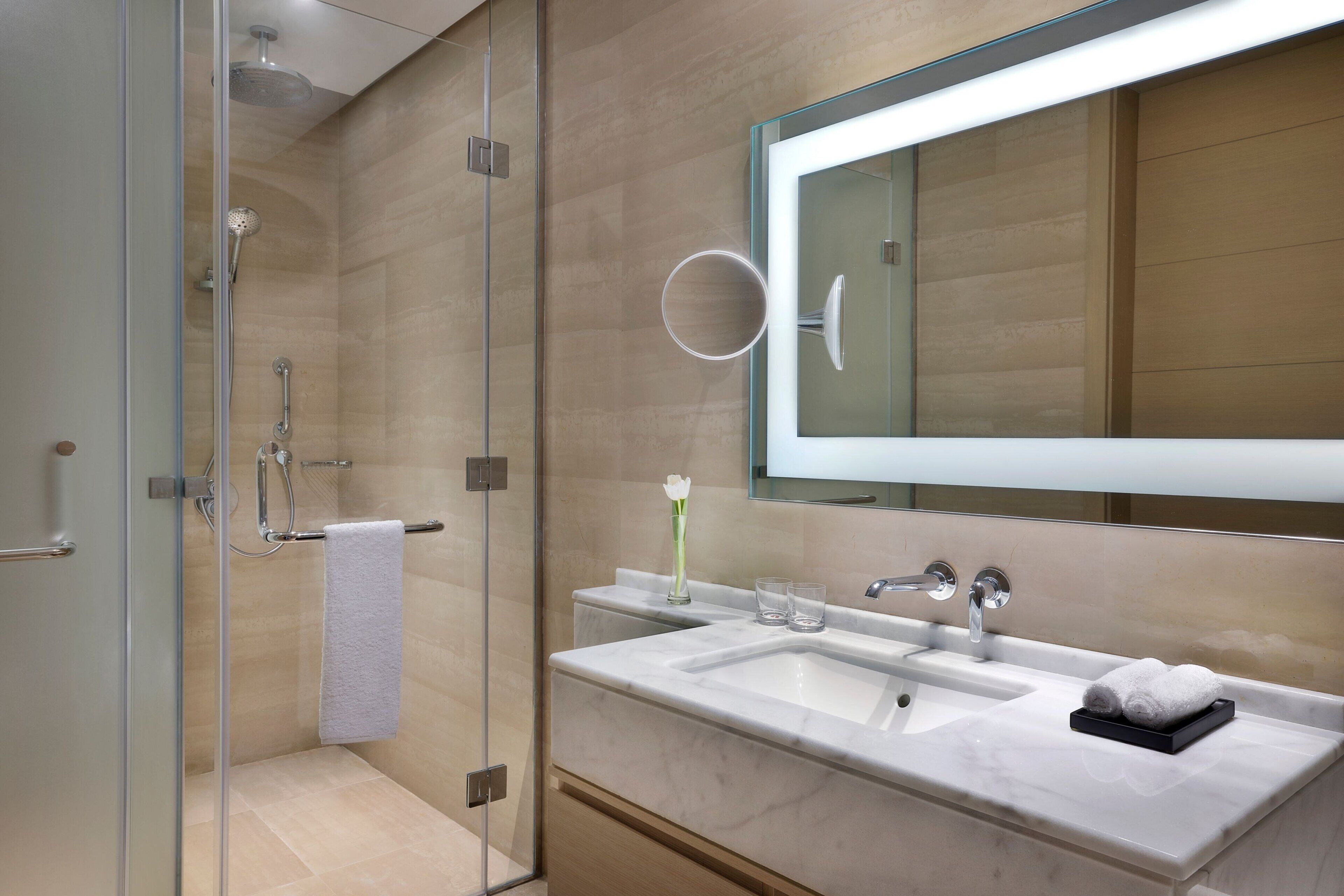 A modern bathroom with a glass-enclosed shower, a large mirror, and a marble sink.