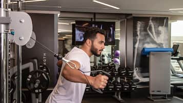 A gym with weightlifting equipment, a television screen, and a treadmill.