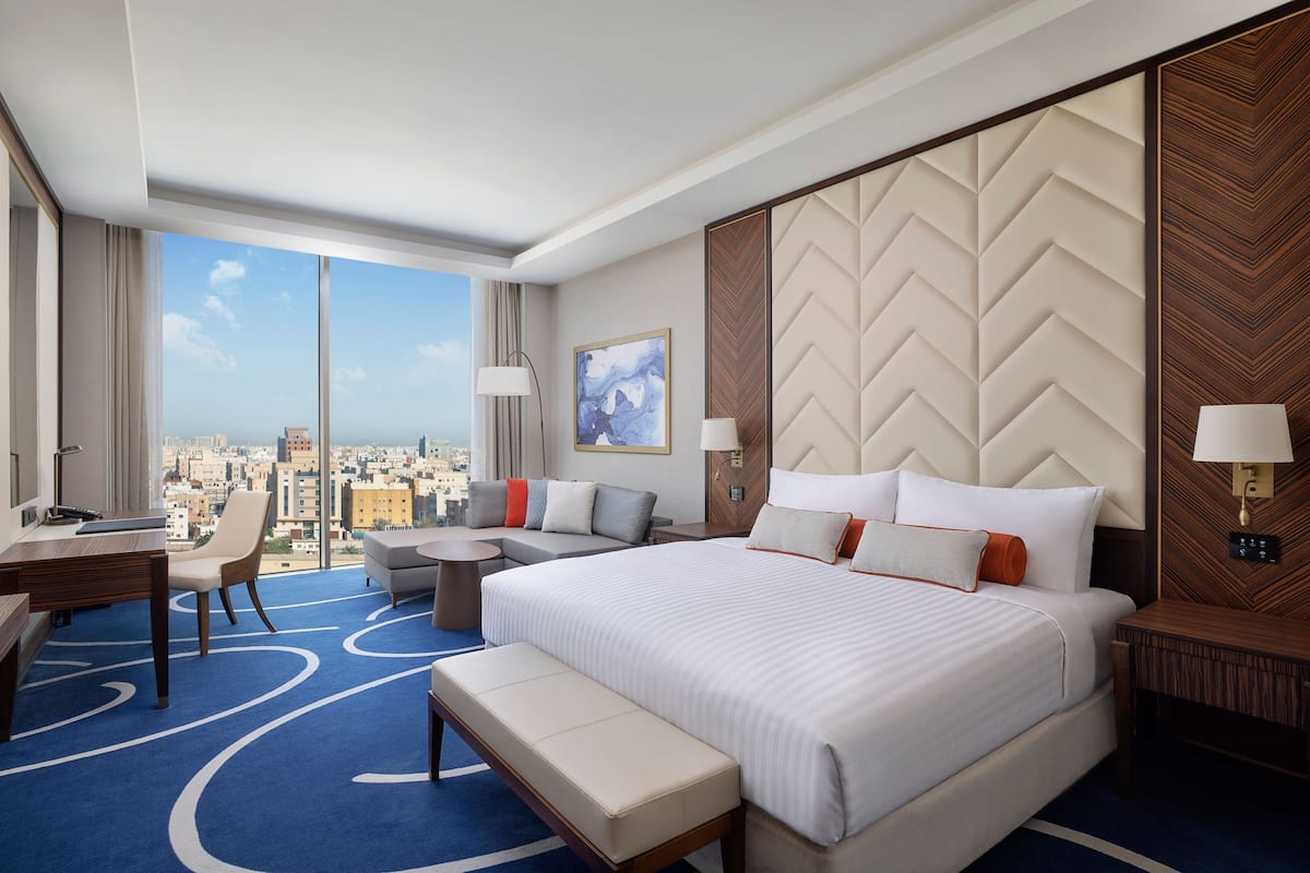 Une chambre d’hôtel avec un grand lit, un bureau, une chaise, une petite table et une vue sur la ville.