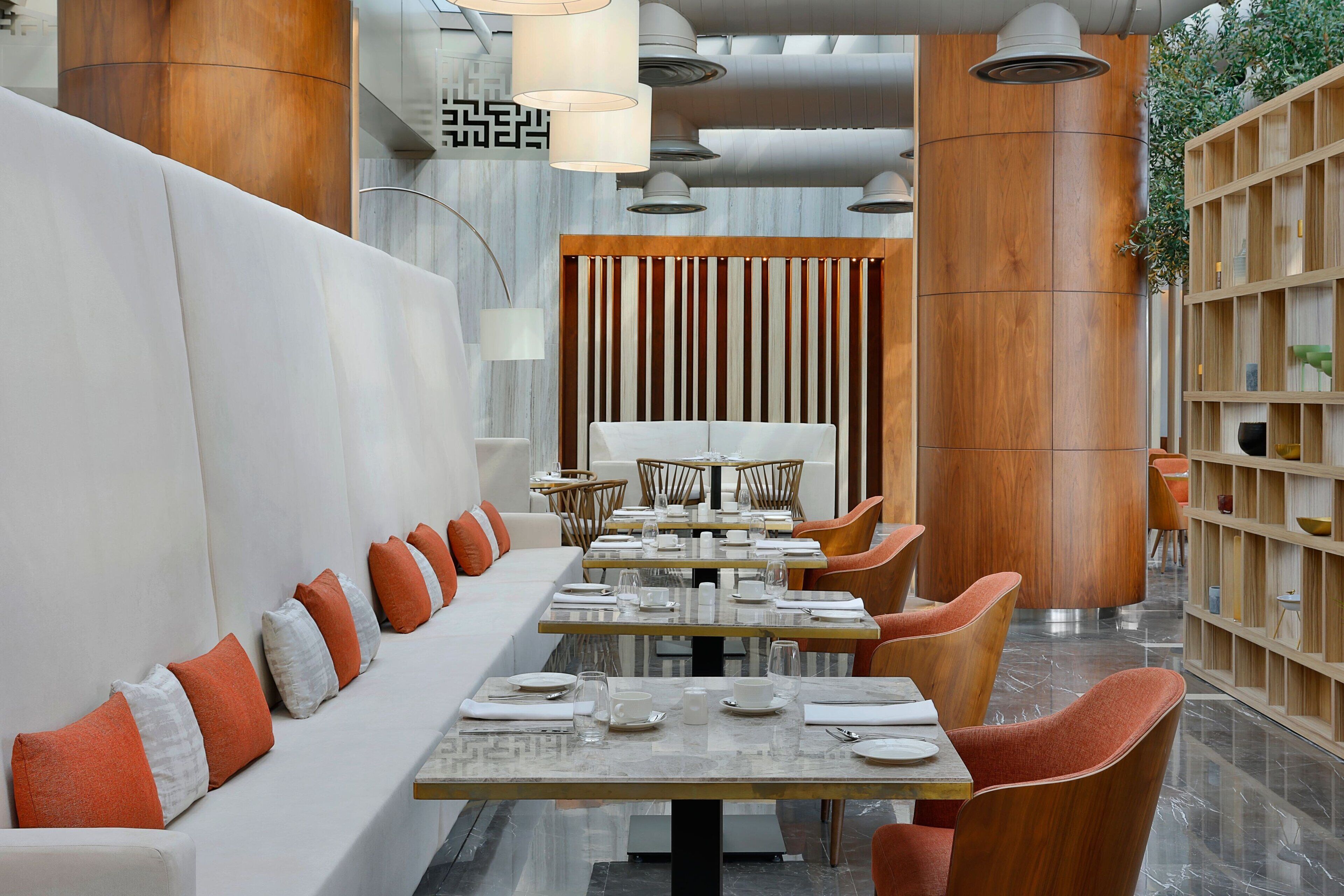 A modern restaurant with a long white bench, wooden chairs, and a central dining table set for service.
