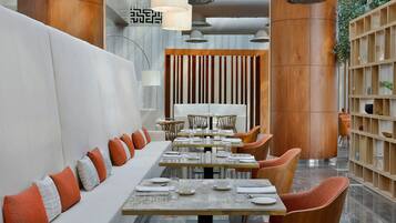A modern restaurant with a long white bench, wooden chairs, and a central dining table set for service.