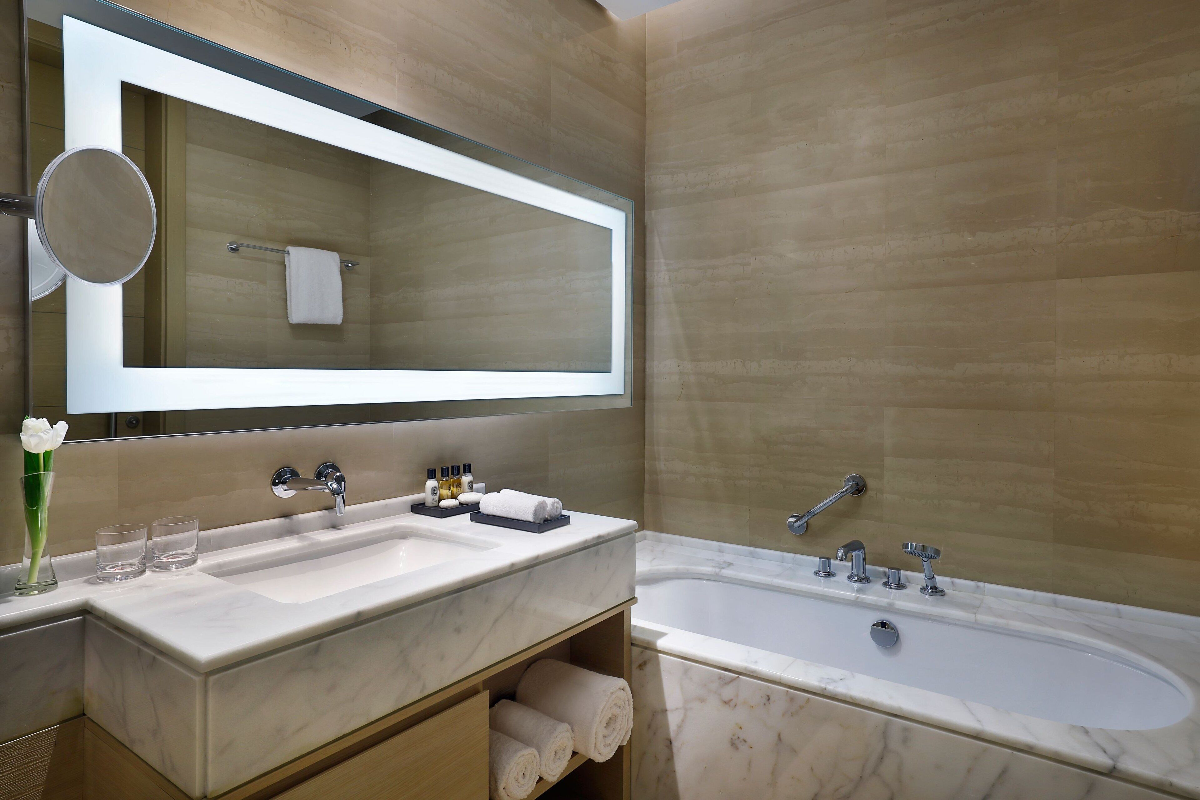 A modern bathroom with a large mirror, two sinks, a bathtub, and a towel rack.