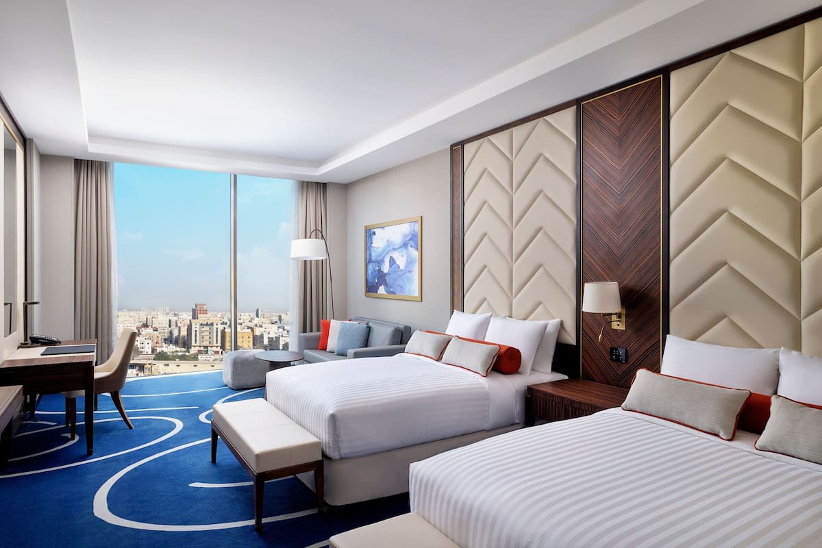 Une chambre d’hôtel avec deux lits, un bureau et une vue sur la ville.