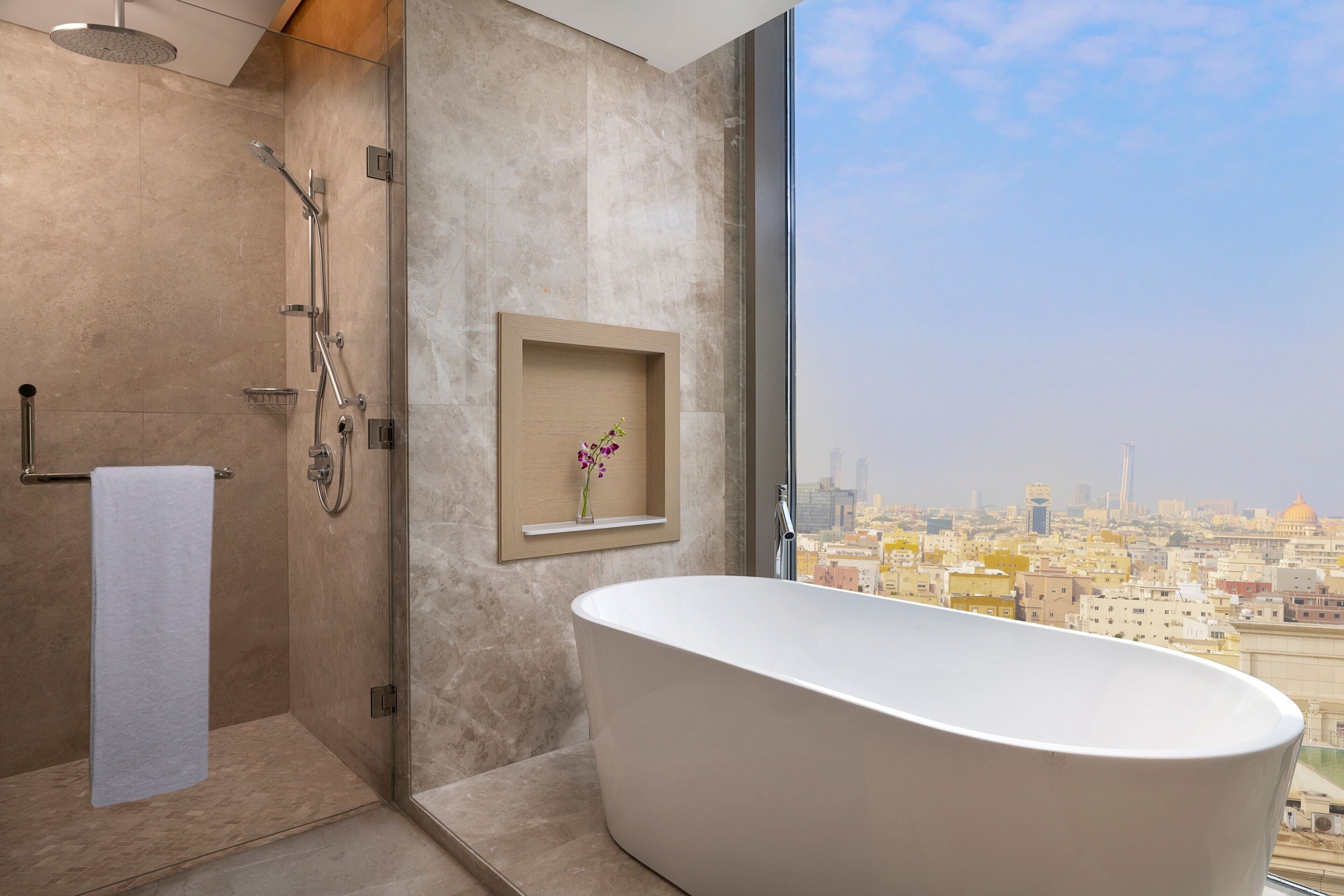 Un baño moderno con una bañera independiente, ducha con mampara de vidrio y vistas a la ciudad.