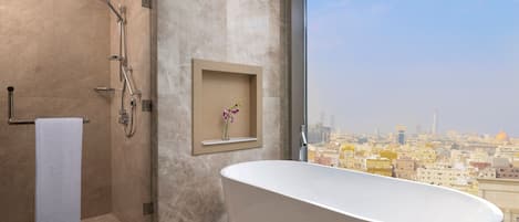 Un baño moderno con una bañera independiente, ducha con mampara de vidrio y vistas a la ciudad.