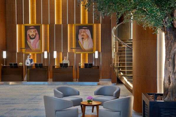 A lobby with a reception desk, two seating areas, a staircase, and a large tree.
