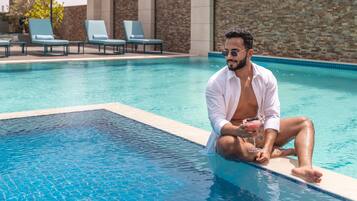 Ein Mann sitzt an einem Pool mit Liegestühlen und einer Steinmauer im Hintergrund.