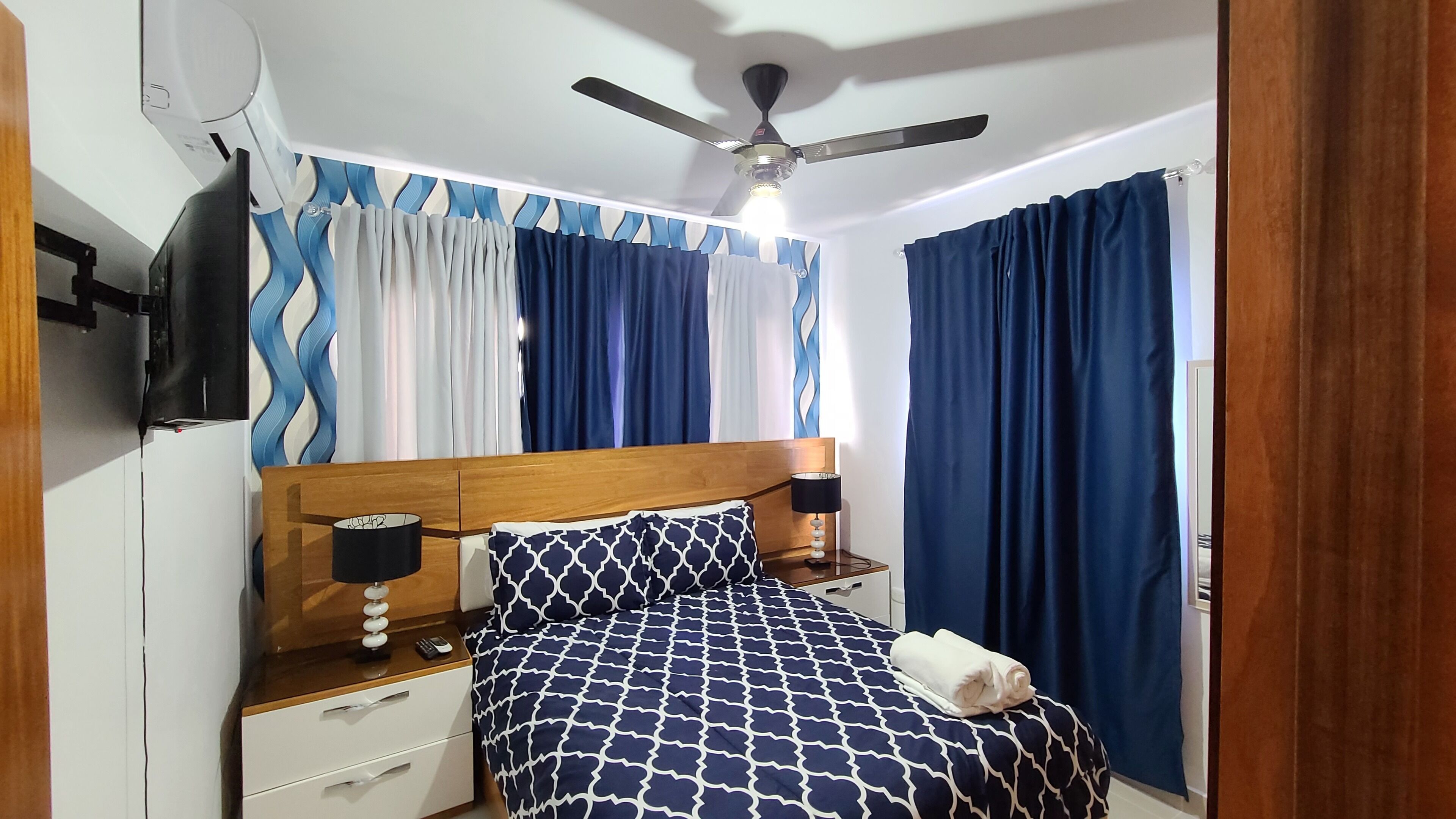 A bedroom with a bed, nightstands, a ceiling fan, and curtains.