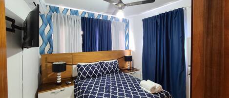 A bedroom with a bed, nightstands, a ceiling fan, and curtains.