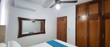 Un dormitorio con cama, ventilador de techo, aire acondicionado, espejo y armarios de madera.