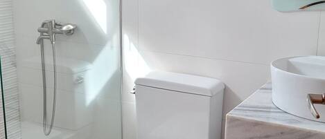 A modern bathroom with a glass shower enclosure, a white toilet, a marble countertop, and a small trash bin.