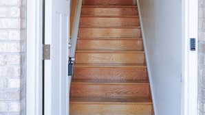 Una escalera de madera que conduce a una habitación con paredes blancas y fachada de ladrillo.