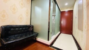 A narrow hallway with a black leather sofa, a sliding glass door, and a wooden door.