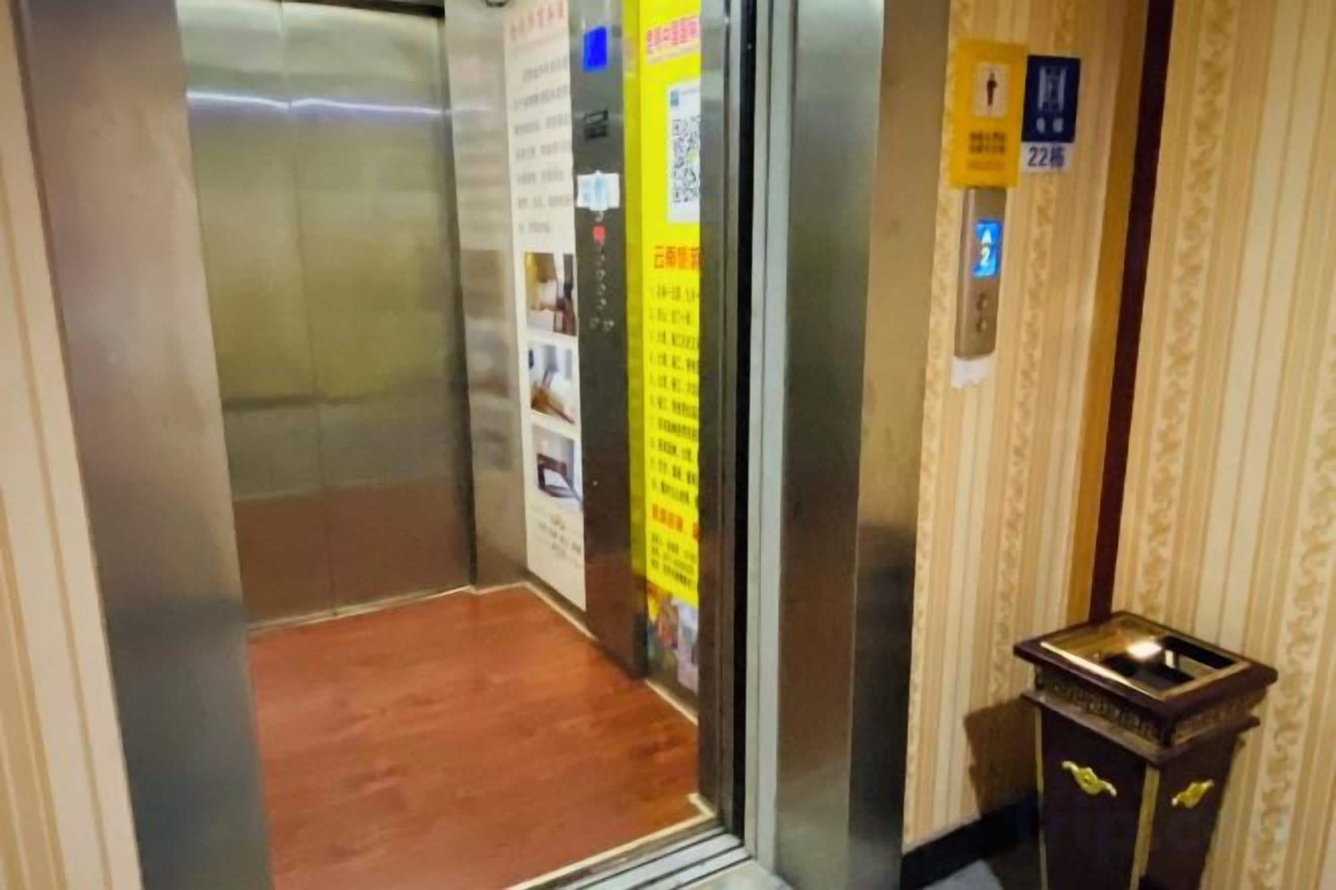 An elevator interior with a wooden floor, informational posters, and a small wooden cabinet with a light fixture.