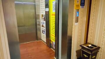 An elevator interior with a wooden floor, informational posters, and a small wooden cabinet with a light fixture.