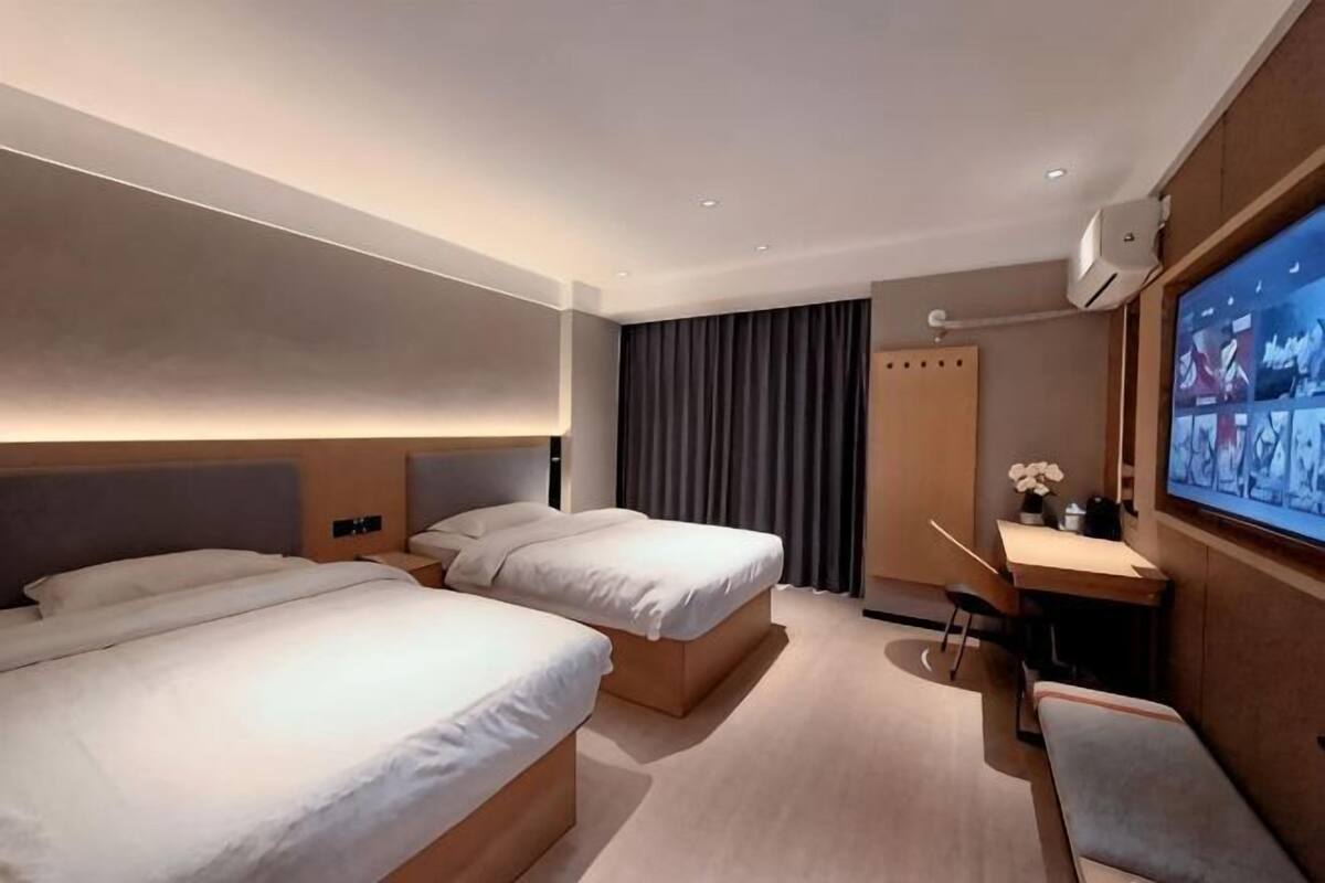 Ein Hotelzimmer mit zwei Betten, einem Schreibtisch mit Stuhl, einem Fernseher und einem Vorhang.