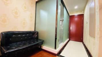 A narrow hallway with a black leather sofa, a sliding glass door, and a red door at the end.