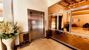 A hotel lobby with a reception desk, an elevator, and a large window with a view of the interior.