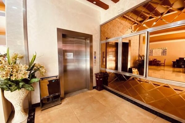 A hotel lobby with a reception desk, an elevator, and a large window with a view of the interior.