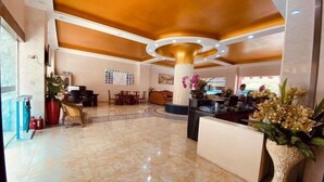 A lobby with a marble floor, a reception desk, a seating area, and a large decorative column.